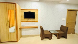 A room with a wooden wardrobe, a mounted TV, a glass-top table, and two brown chairs. - Hotel Manish International (Varanasi)