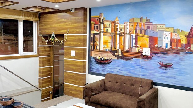 A modern living room with a sofa, a coffee table, and a large cityscape painting on the wall. - Hotel Manish International (Varanasi)
