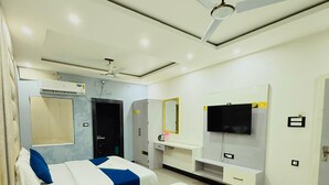 A hotel room with two beds, a TV, a ceiling fan, an air conditioning unit, and a small trash bin. - Hotel Manish International (Varanasi)