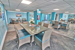 A spacious indoor area with wicker furniture, a glass table, and a blue wall. - Oceanfront-Waterpointe 1 Unit 702-Windy Hill Beach-Sleeps 6-3br/2ba-Pools (North Myrtle Beach)