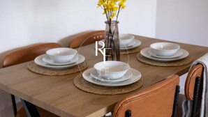 Ett matbord dukat med vita skålar och tallrikar, en vas med gula blommor och en läderstol.