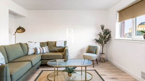 A modern living room with a green sofa, a striped armchair, a glass coffee table, and a floor lamp. - The Den on Catto Drive (Peterhead)