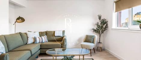 A modern living room with a green sofa, a striped armchair, a glass coffee table, and a floor lamp.