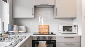 A modern kitchen with a microwave, oven, and a wooden cutting board with a suitcase design. - The Den on Catto Drive (Peterhead)