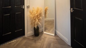 En hall med två svarta dörrar, en spegel och en vas med torkat pampasgräs.