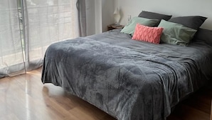 Un dormitorio con una cama grande, una ventana con vista a la vegetación y una puerta corrediza de vidrio.