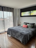 Un dormitorio con una cama grande, una ventana con vista a la vegetación y una puerta corrediza de vidrio.
