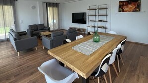 Una sala de estar moderna con una mesa de comedor de madera, sofás grises y un televisor montado en la pared.