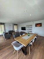 Una sala de estar moderna con una mesa de comedor de madera, sofás grises y un televisor montado en la pared.