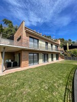 Una casa moderna de dos pisos con techo plano, ventanas amplias y un balcón.