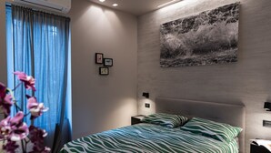 A modern bedroom with a zebra-patterned bedspread, a large abstract painting on the wall, and a window with blue curtains.