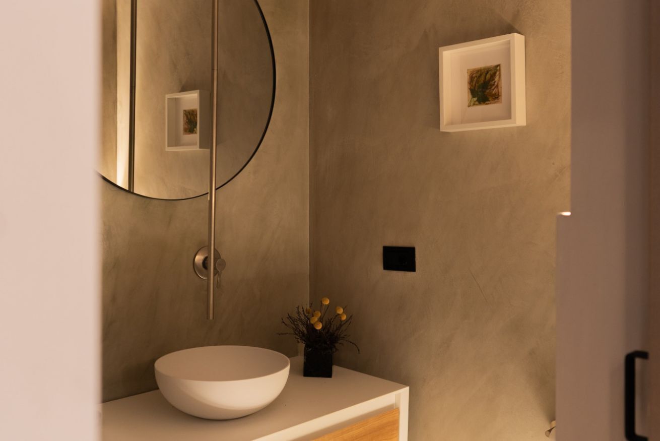 A modern bathroom with a large mirror, a round sink, and a small potted plant.