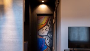 A hallway with a colorful abstract mural on the wall, a flat-screen TV on a stand, and a door with a light fixture above it.