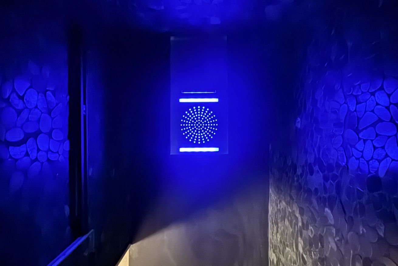 Een smalle gang met aan de ene kant een stenen muur en aan de andere kant een blauw verlichte muur.