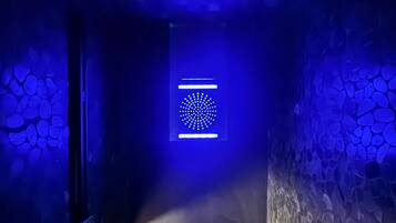 Een smalle gang met aan de ene kant een stenen muur en aan de andere kant een blauw verlichte muur.
