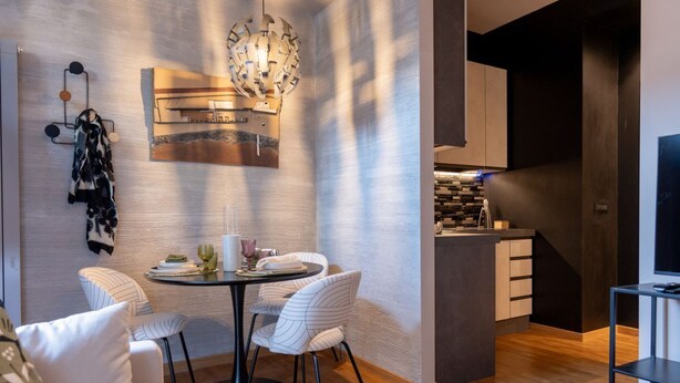 A modern kitchen with a central island, a dining area with striped chairs, and a hanging light fixture.