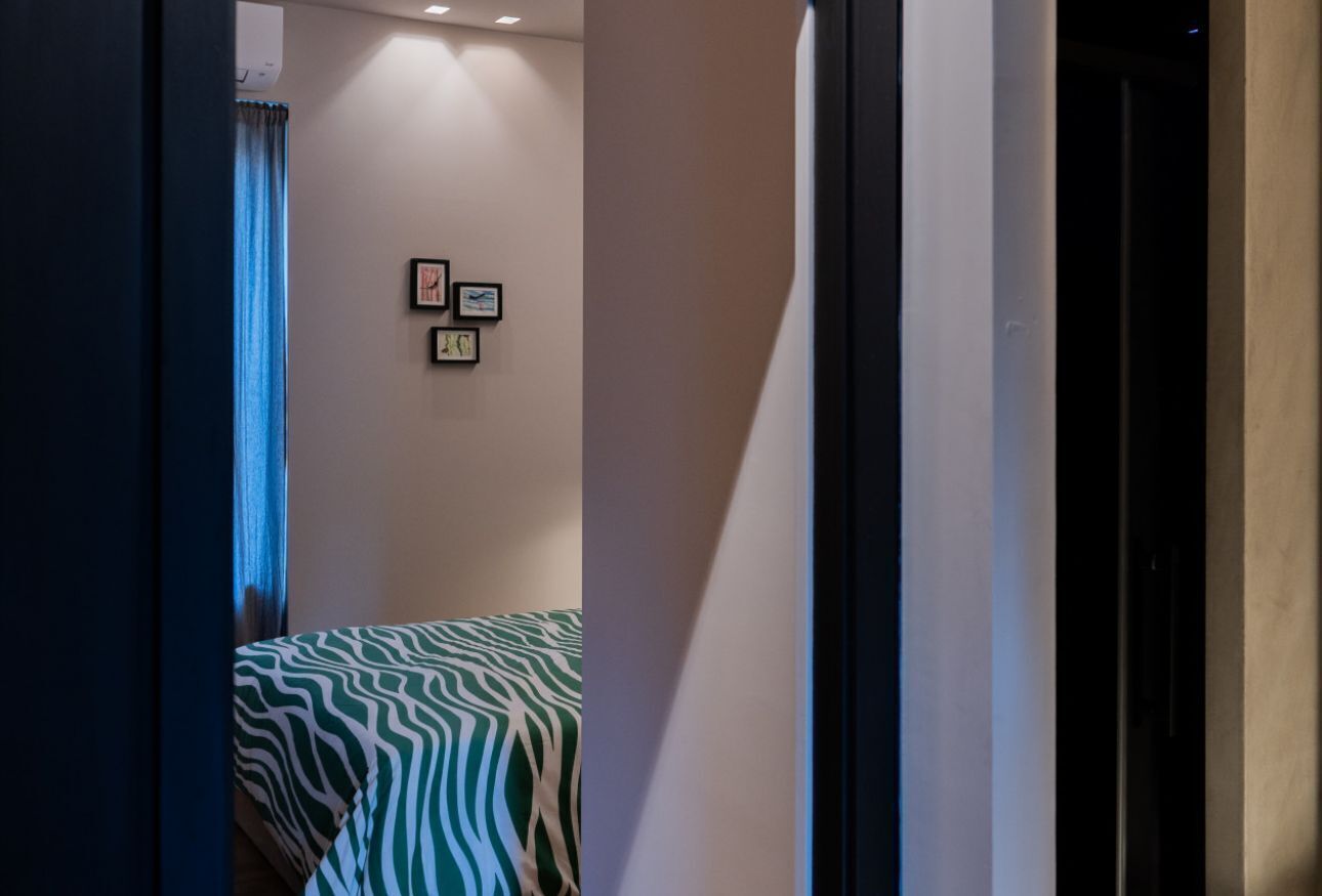A narrow hallway with a bed at the end, framed pictures on the wall, and a blue curtain.