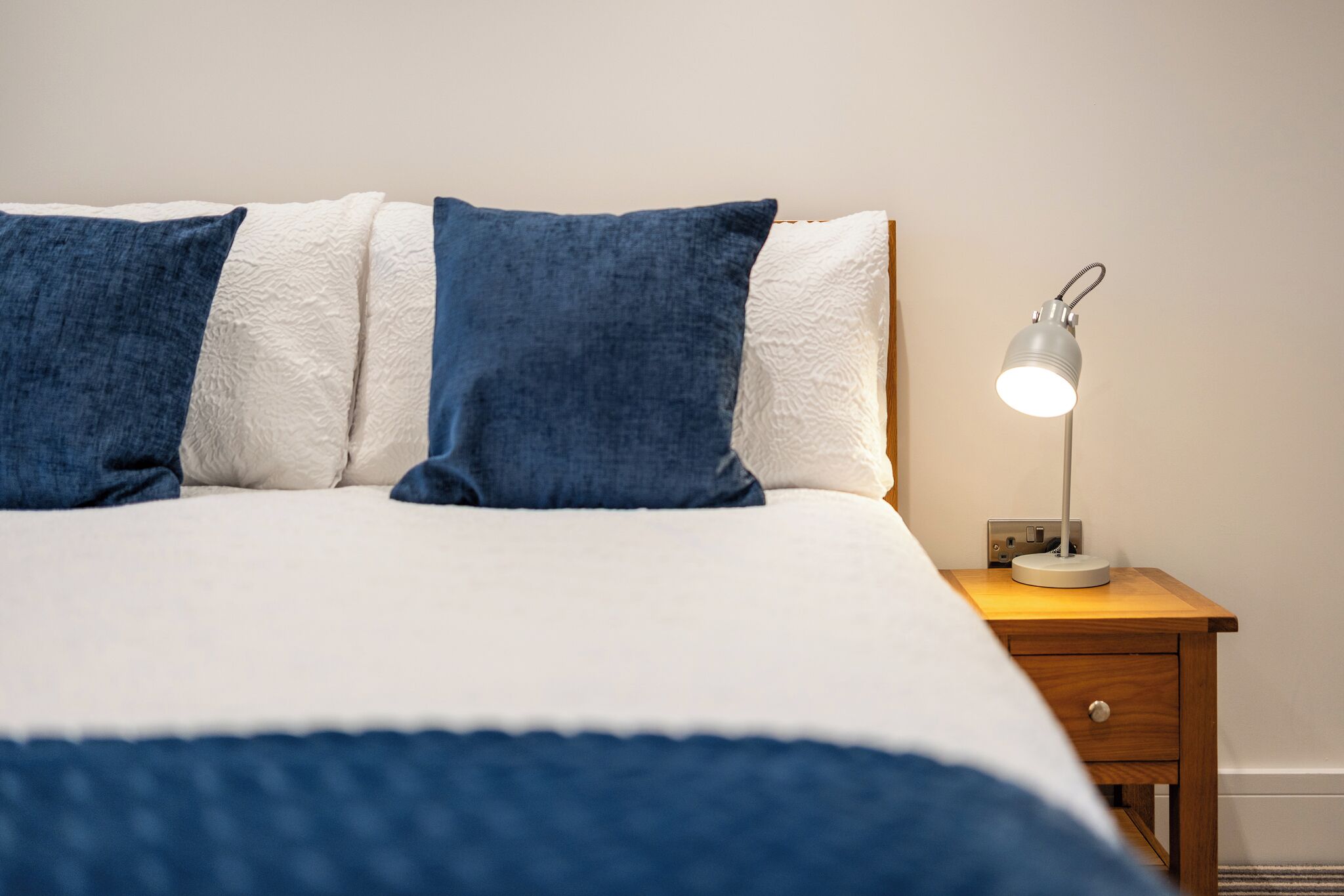 A neatly made bed with blue and white pillows, a bedside lamp, and a wooden nightstand.