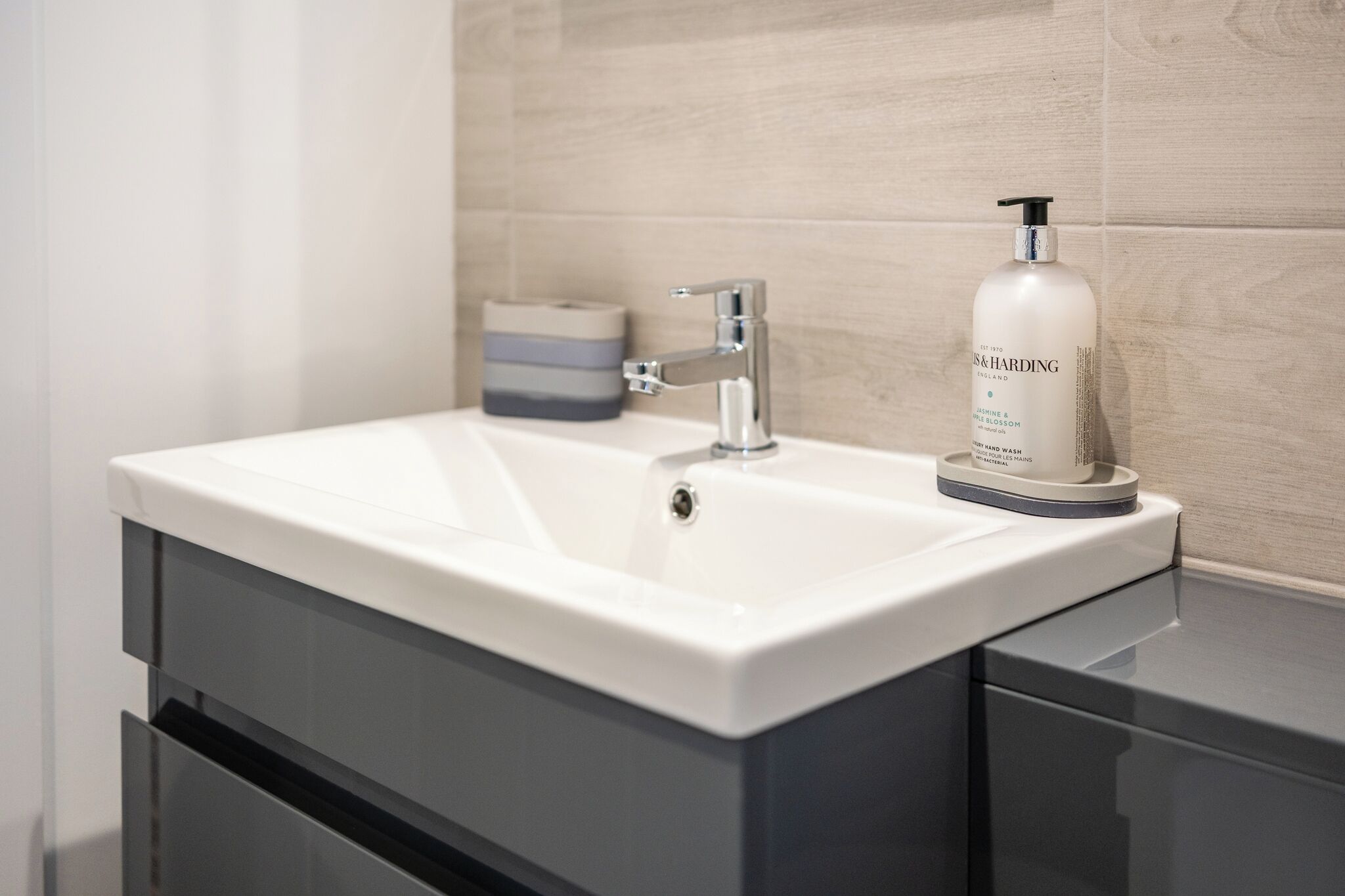 Een moderne badkamer met een witte wastafel, een zilveren kraan en een handzeepfles.