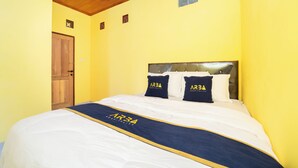 Una habitación de hotel con techo de madera, cama con ropa de cama blanca y detalles azul marino, y pared amarilla.