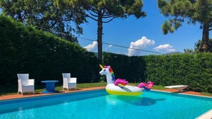 Une piscine avec un flotteur en forme de licorne, des chaises blanches et une terrasse carrelée.