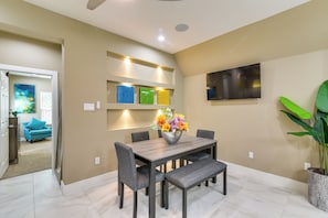 A dining area with a wooden table, gray chairs, and a bench. There is a flower vase on the table, and a potted plant to the side. - Pool Table & Fenced Yard: Home 5 Mi to NRG Stadium (Houston)