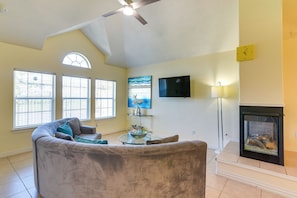 A living room with a gray sofa, a glass coffee table, a fireplace, and a TV mounted on the wall. - Fenced Yard, < 2 Mi to Dtwn Houston: Family Home! (Houston)