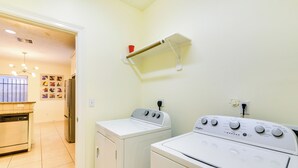 Une buanderie équipée de deux machines à laver blanches, d’une petite étagère sur laquelle se trouve une tasse rouge, et d’un sol carrelé.