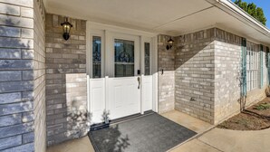 Una casa con puerta blanca, dos ventanas con vidrios en forma de estrella y fachada de ladrillo.