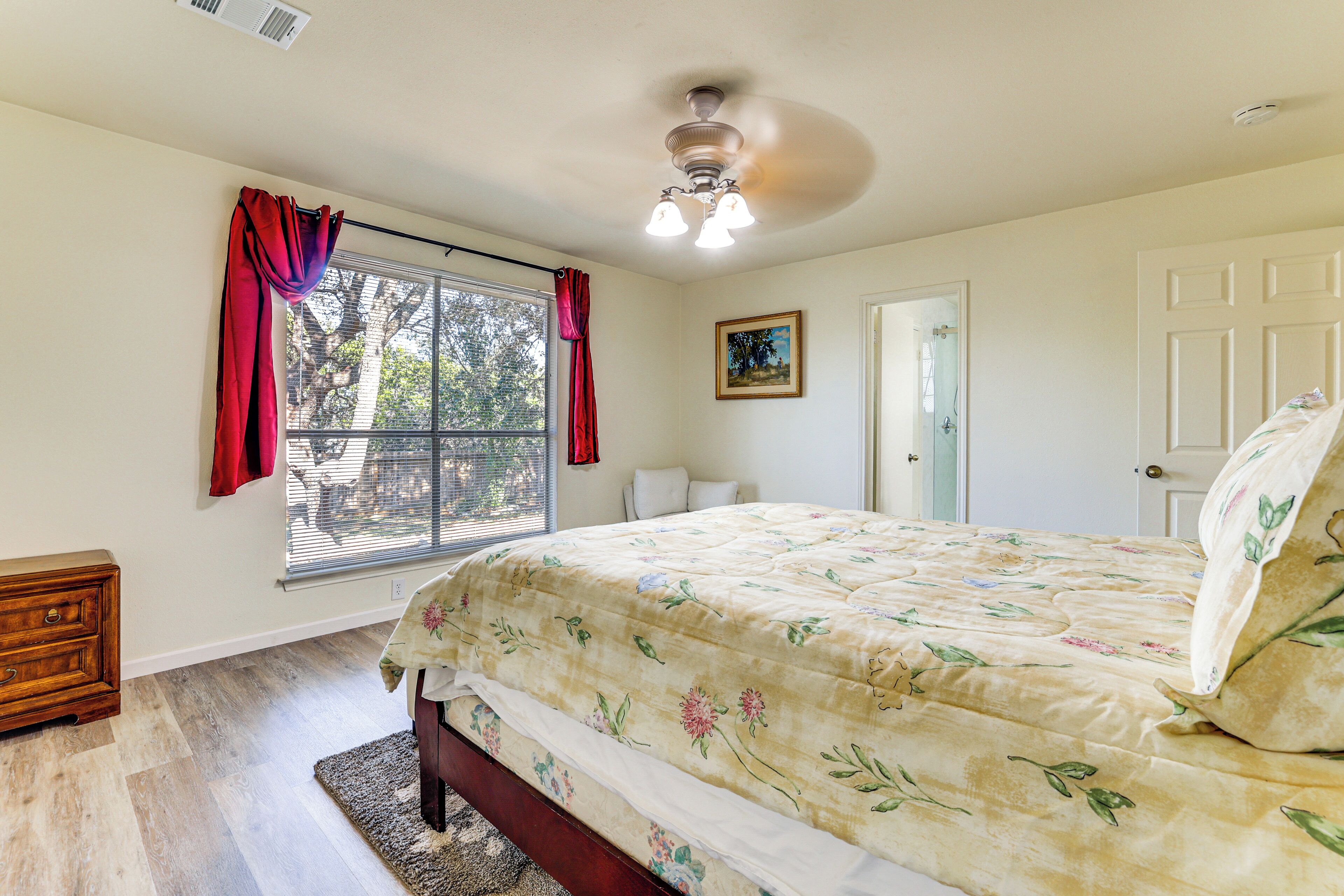 Un dormitorio con cama, ventana con cortinas, puerta y ventilador de techo.