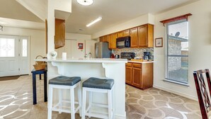 Una cocina con armarios de madera, un microondas y un refrigerador. Hay dos taburetes de bar con asientos acolchados.