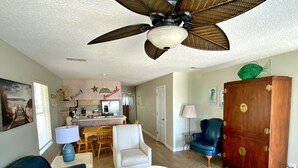 Un salon doté d’un ventilateur de plafond, un coin repas avec une table et des chaises, une cuisine équipée d’appareils électroménagers et un meuble en bois.