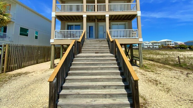 Une maison à deux étages située en bord de mer, avec un escalier en bois menant à un balcon.