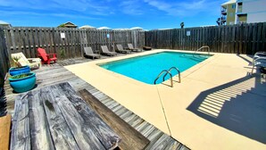 Une piscine rectangulaire entourée d’une terrasse en bois, d’une clôture en bois et de chaises longues.