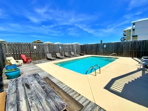 Ein rechteckiger Swimmingpool mit umlaufender Holzterrasse, einem Holzzaun und Liegestühlen.