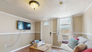 Ein gemütliches Wohnzimmer mit Fernseher, Couchtisch aus Holz, einer Couch mit Kissen, einem gemusterten Teppich und einer Tür mit Fenster.