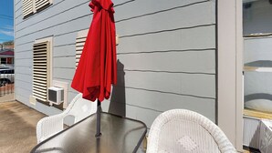 A patio with a table and chairs, a red umbrella, and a building with horizontal siding. - 2-story Galveston Getaway w/ Balcony & Patio (Galveston)