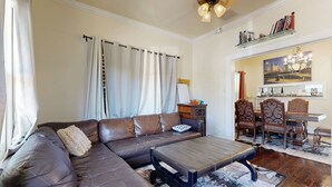 A living room with a sectional sofa, a coffee table, and a dining area with chairs and a table. - 2-story Galveston Getaway w/ Balcony & Patio (Galveston)