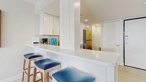 Een moderne keuken met witte kasten, een centraal eiland met barkrukken en een koelkast.
