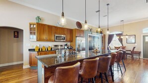 A modern kitchen with wooden cabinets, stainless steel appliances, and a central island with bar stools. - 4BR Home w/ Outdoor Patio & In-ground Pool (Rotonda West)