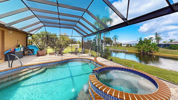 A swimming pool with a glass enclosure, a hot tub, and a patio area with lounge chairs and a slide. - 4BR Home w/ Outdoor Patio & In-ground Pool (Rotonda West)