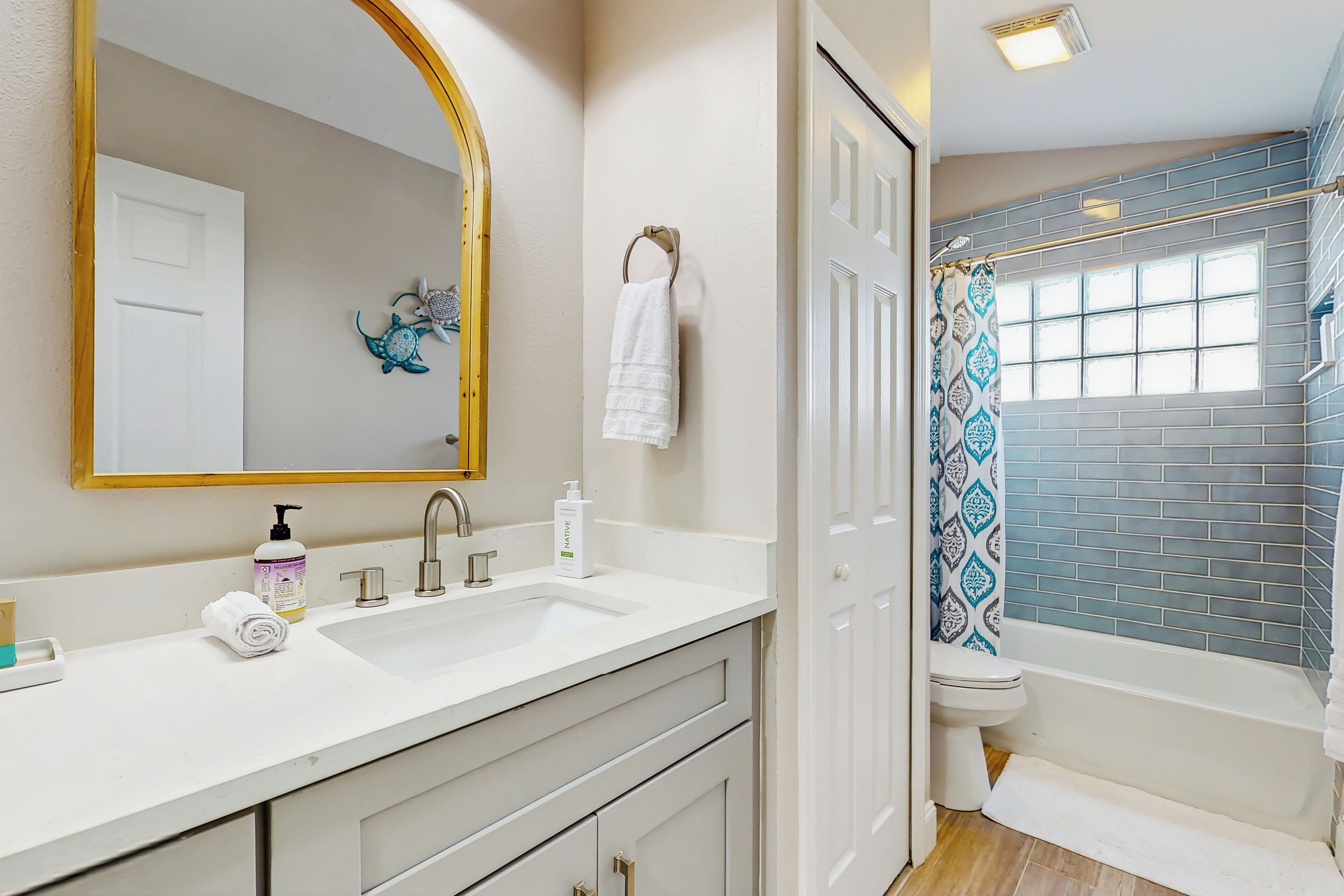 A bathroom with a white sink, a mirror, a towel rack, and a shower with a blue patterned curtain.