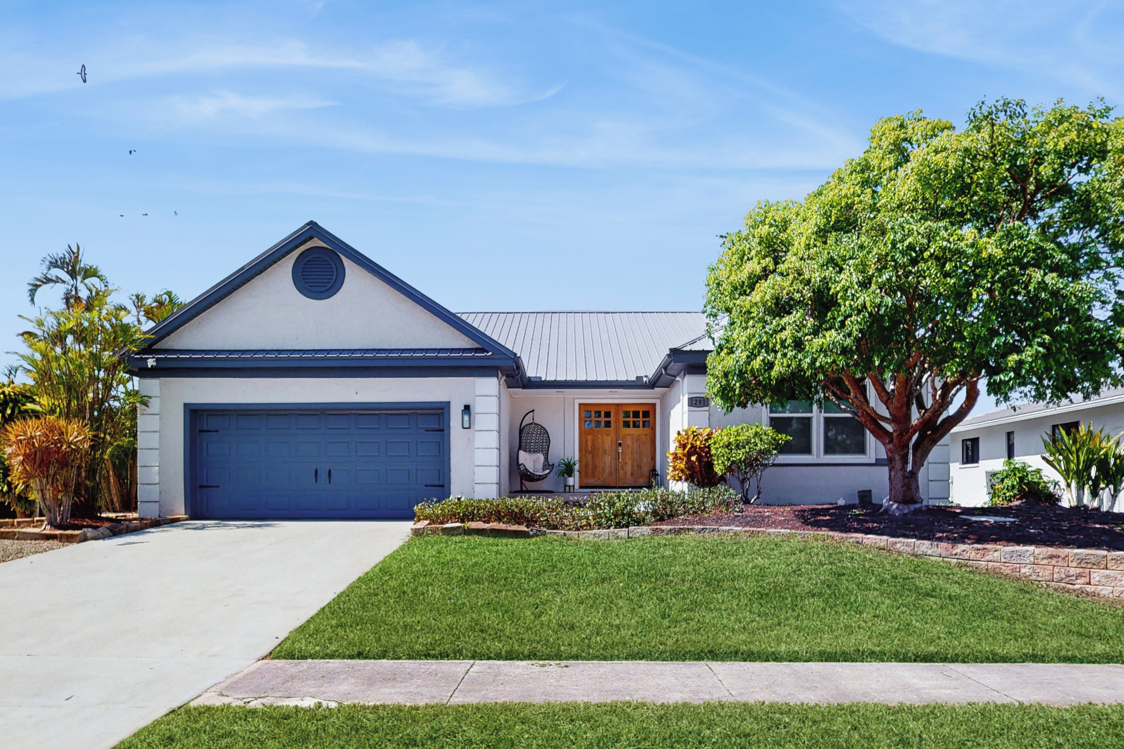 A single-story house with a garage, a front porch, and a large tree.