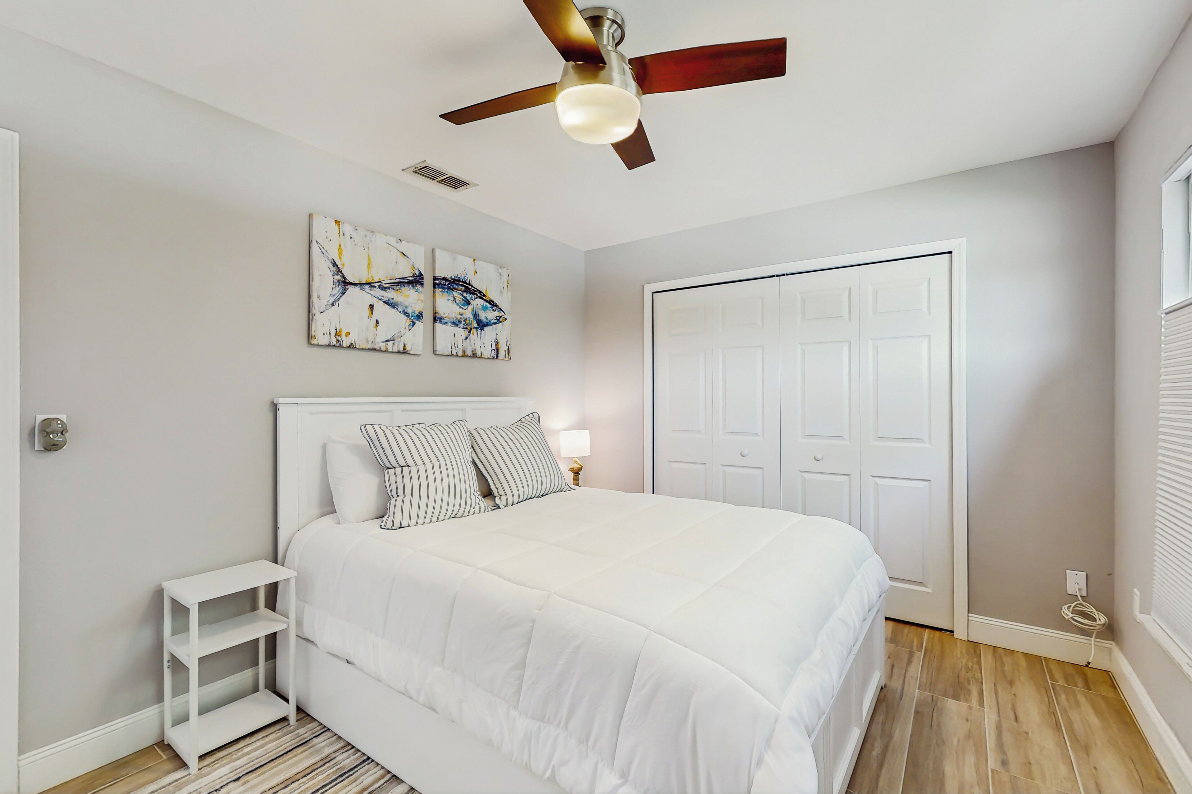 Quarto com cama, ventilador no teto, porta branca e obras de arte na parede.