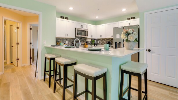 Una cocina moderna con armarios blancos, una isla central con taburetes, un microondas de acero inoxidable y un refrigerador.