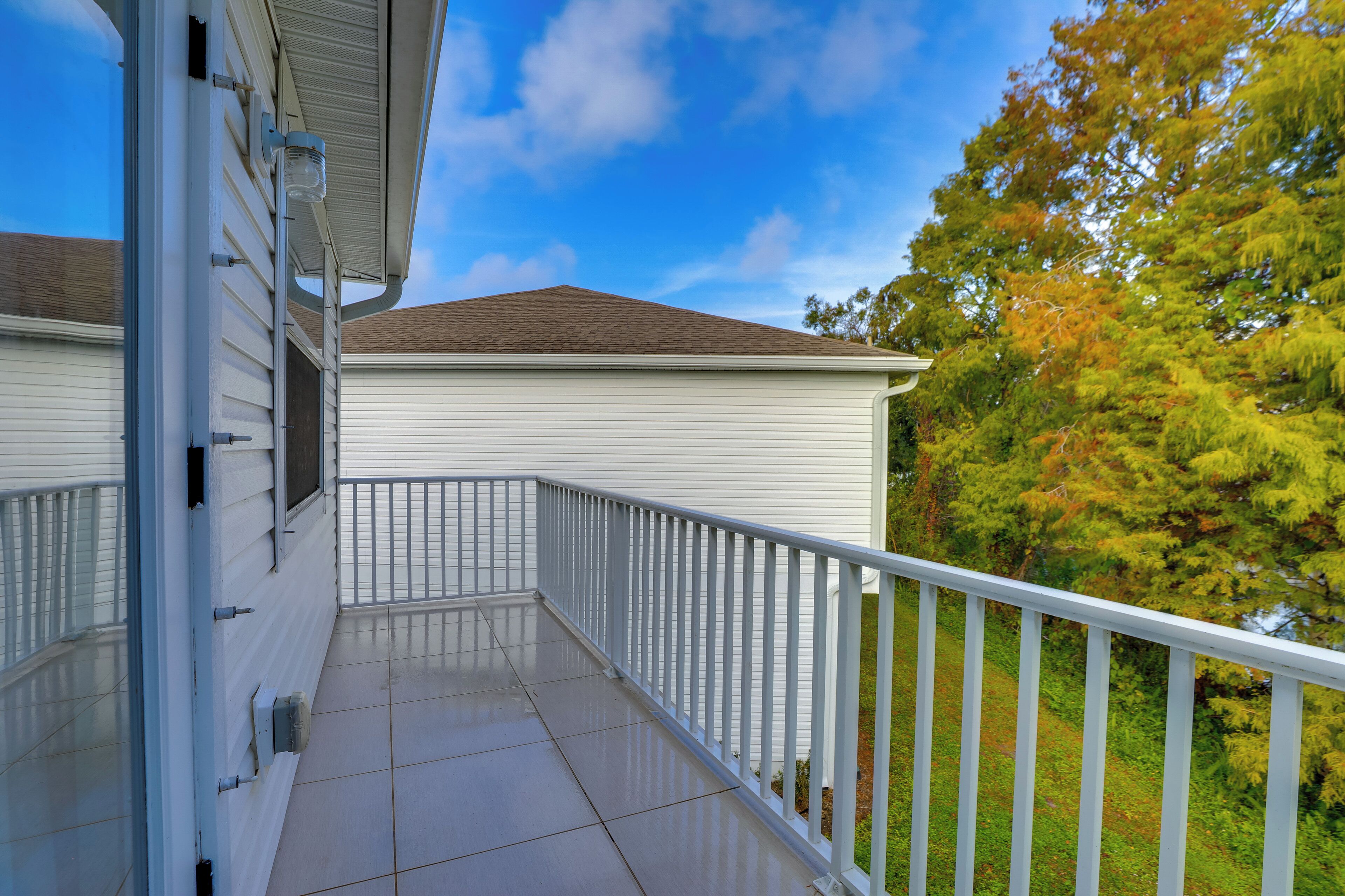 A balcony with a white railing, a tiled floor, and a view of trees and a building.