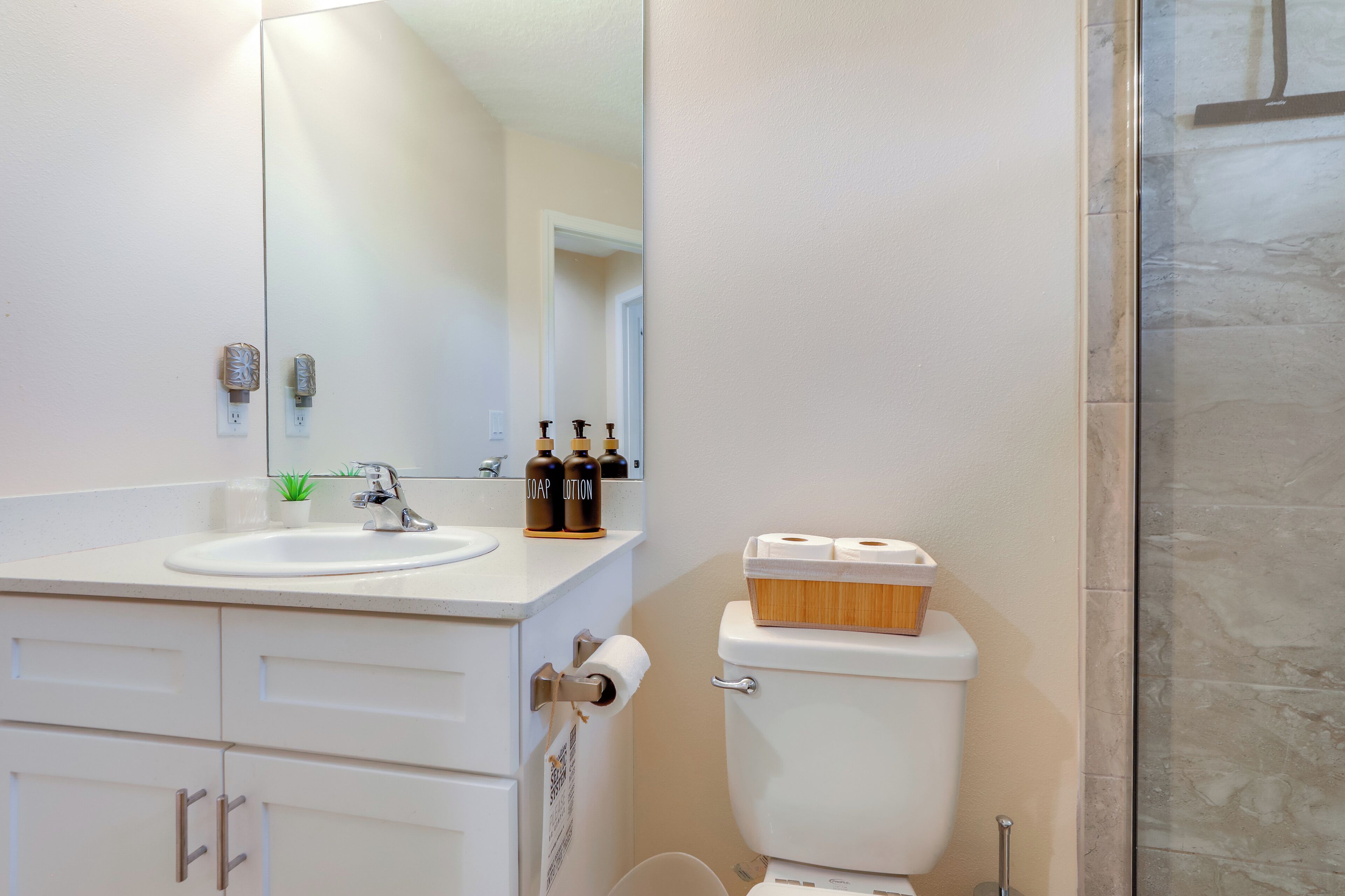A bathroom with a white sink, mirror, toilet, and shower.