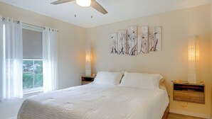 Un dormitorio con una cama grande, ventilador de techo, ventana con cortinas y decoración en la pared.