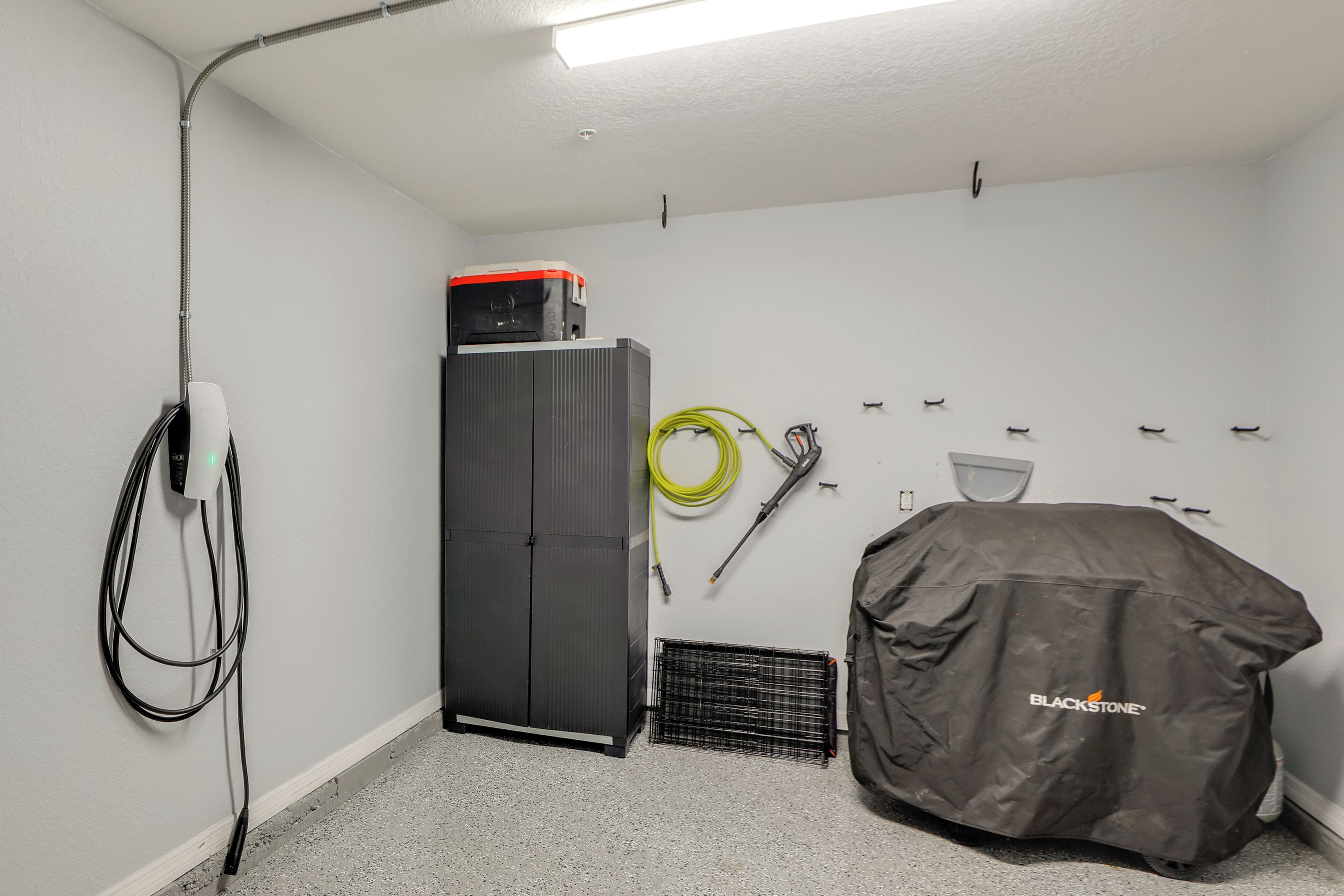 Une pièce utilitaire avec un meuble gris, un objet recouvert d’une housse et divers outils accrochés au mur.