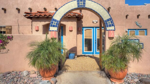 A building with a distinctive arched entrance, a blue door, and terracotta pots with plants. - 3 BR Home, Private Pool, Close to Event Venues (La Quinta)